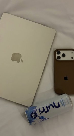 White laptop, brown phone, and drink can on white sheets.