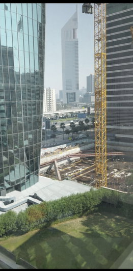 Cityscape with tall buildings, construction crane, and greenery in foreground.