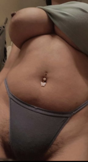 Woman with belly button piercing wearing gray thong, showing midriff and pubic area.
