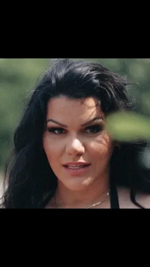 Woman with dark hair and makeup, wearing a black top, outdoors.