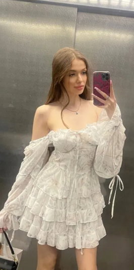 Woman in white ruffled dress taking mirror selfie indoors.