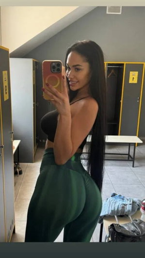 Woman with long dark hair taking mirror selfie in locker room.