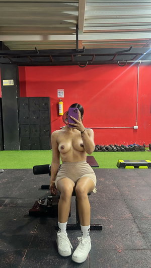 Fit woman topless in beige shorts and sneakers in gym.