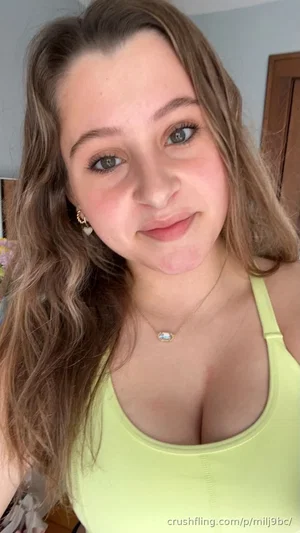 Woman with wavy brown hair in a lime green tank top, smiling at camera indoors.