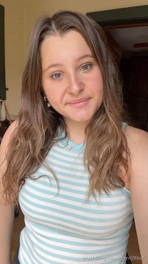 Woman with long brown hair wearing a blue and white striped tank top indoors.