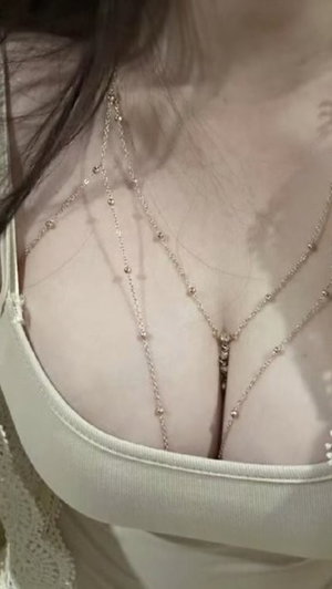 Woman in white top with body chain necklace, indoor setting.