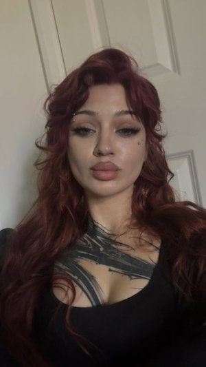 Woman with red hair and tattoos wears black top, indoors.