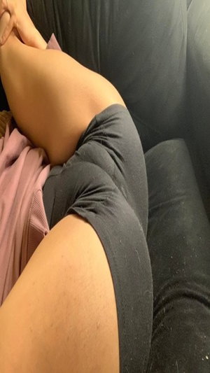 Woman in dark shorts and pink top sitting on black couch, legs crossed.