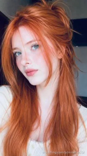 Woman with long red hair and blue eyes wearing a white top, indoors.