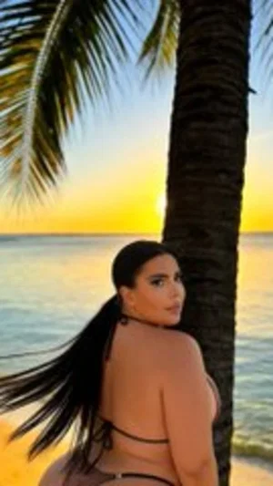 Woman in black bikini posing by palm tree at beach sunset.