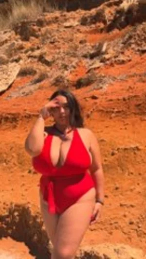 Woman in red swimsuit standing on red rocky terrain outdoors.