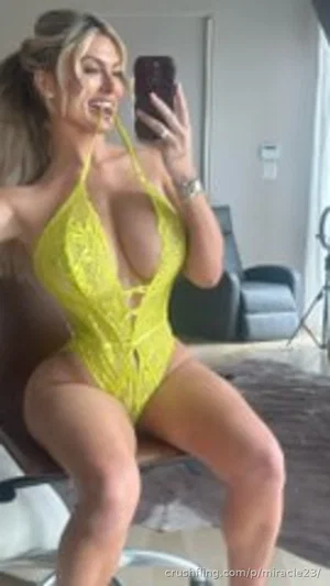 Woman in yellow lace bodysuit taking mirror selfie indoors.