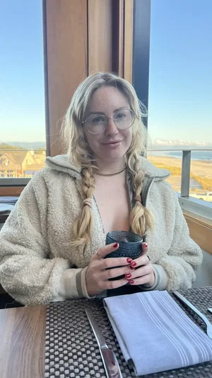 Blonde woman with glasses and braids in fleece jacket at table.