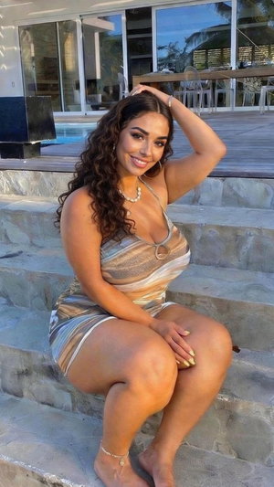 Woman in striped dress sits on stone steps near pool, smiling at camera.