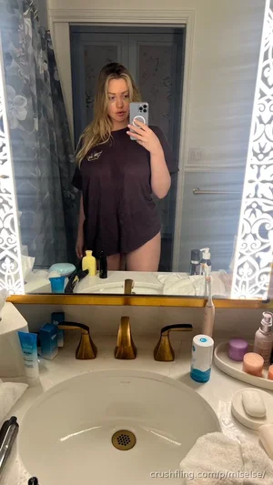 Woman in dark t-shirt and underwear takes mirror selfie in bathroom.