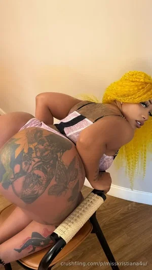 Woman with yellow wig and tattoos in lingerie posing on a chair indoors.