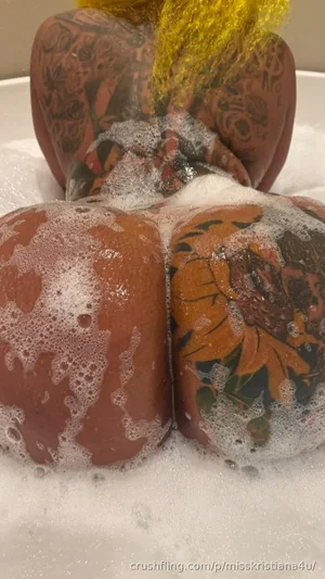 Person with tattooed buttocks in a bubble bath, back view, indoor setting.