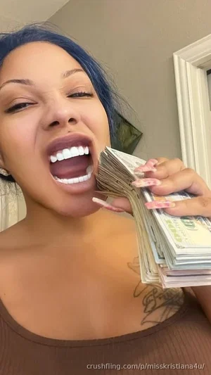 Woman with blue hair and brown top holding cash, indoors.