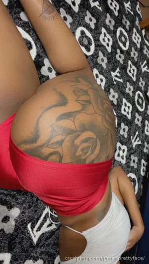 Woman with tattooed buttocks wearing red underwear and white top, lying on patterned blanket.
