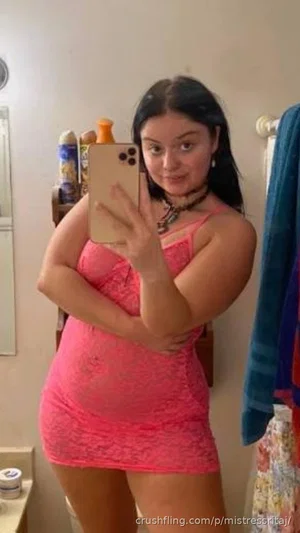 Woman in pink lace dress taking mirror selfie in bathroom.