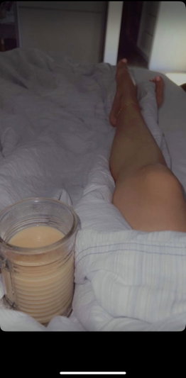 Person's leg on bed with glass of drink, covered in white sheets.