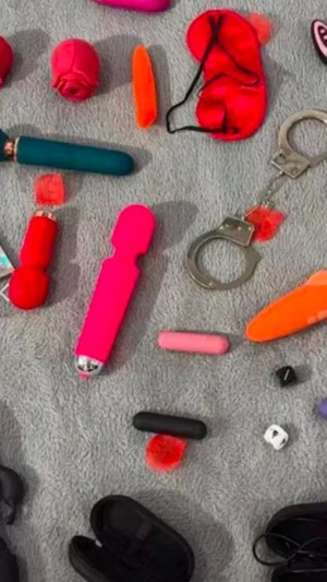 Various colorful sex toys and handcuffs arranged on a gray carpet.