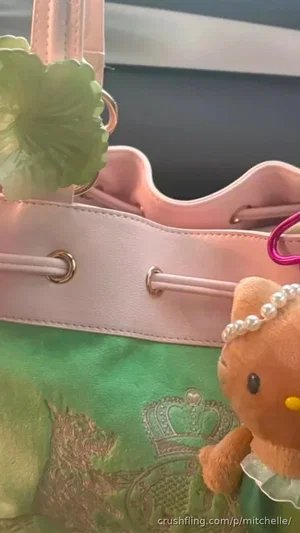 Pink and green bucket bag with Hello Kitty plush charm and floral embellishment.