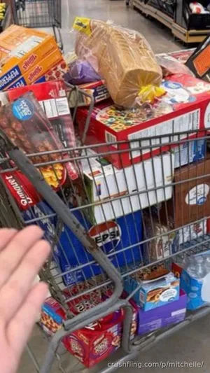Hand holding a shopping cart filled with groceries in a store aisle.