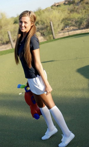Woman with blonde hair in navy top, white shorts, socks on golf course.