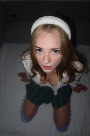 Woman with blonde hair in white top and plaid shorts on bed, wearing white headband and striped