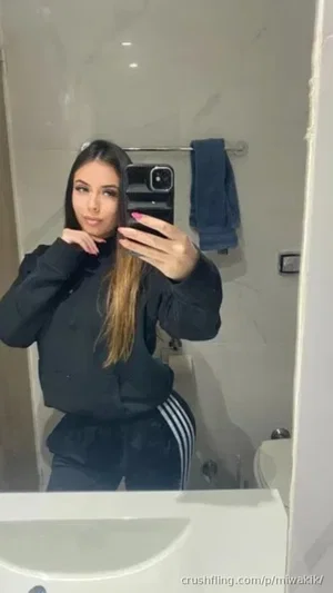 Woman in black tracksuit taking mirror selfie in bathroom.