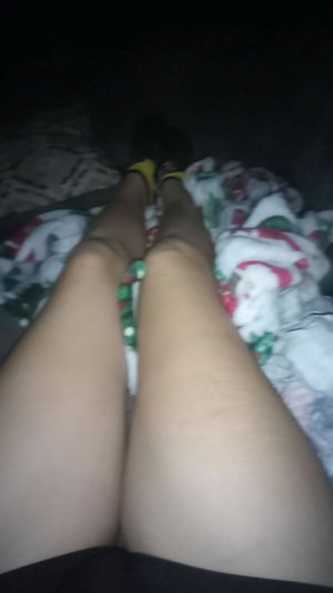 Woman's slim legs in yellow heels and black shorts on bed.
