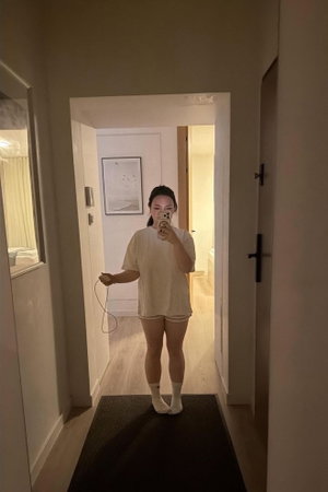 Woman in t-shirt and shorts taking mirror selfie in hallway