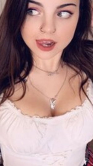 Brunette in white lace top with necklace, indoor selfie.