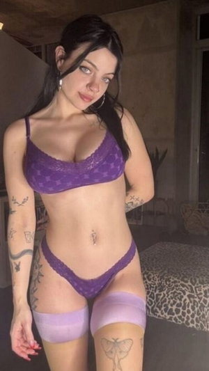 Dark-haired woman in purple lace lingerie in loft bedroom.