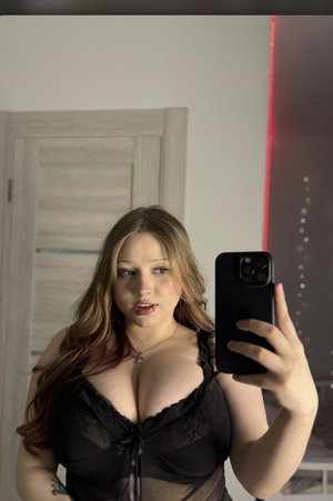 Curvy woman in black lingerie taking mirror selfie indoors.