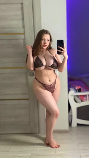 Woman in brown lingerie taking mirror selfie in bedroom.
