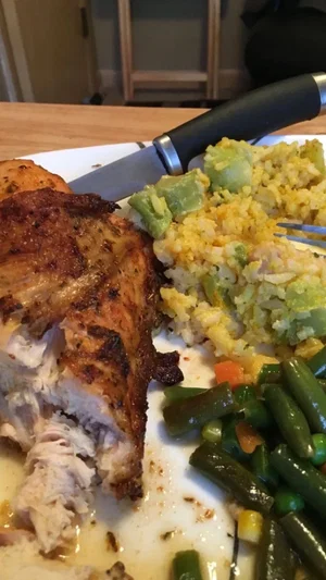 Plate of roasted chicken, rice, and green beans on a wooden table.