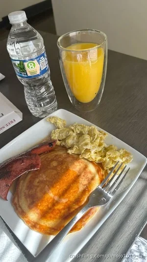 Breakfast plate with pancakes, scrambled eggs, sausage, water bottle, and orange juice on table.