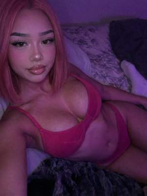 Woman with pink hair in pink lingerie on bed.
