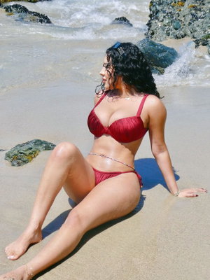 Woman in red bikini sitting on sandy beach near ocean waves.
