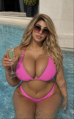Woman in pink bikini holding champagne glass in pool, blonde hair, sunglasses.