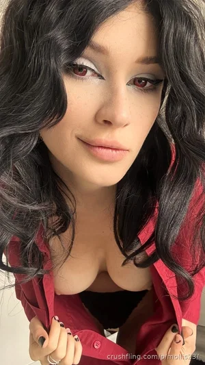 Woman with dark wavy hair, wearing red shirt open over black bra, posing indoors.