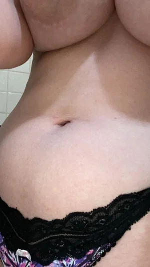 Woman in black lace underwear, showing midriff and lower chest, indoor setting.