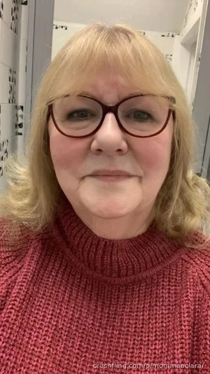 Woman with blonde hair and glasses wearing a red turtleneck sweater indoors.