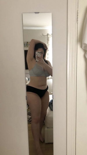 Curvy woman in gray bra and black panties in bedroom mirror selfie.