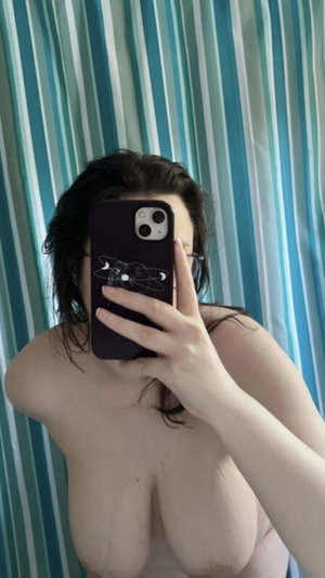 Topless woman with wet dark hair in bathroom selfie.
