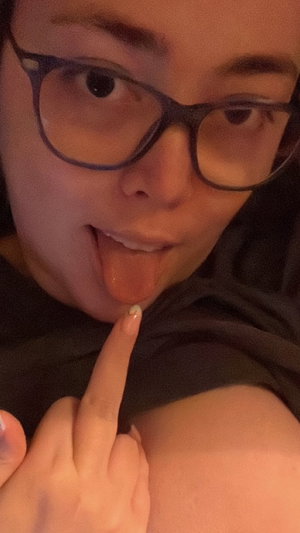 Woman with glasses sticking tongue out in close-up selfie.