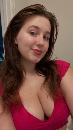 Woman with brown hair in pink top, smiling indoors.