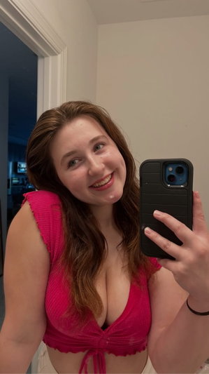 Woman in pink top taking mirror selfie indoors, smiling.